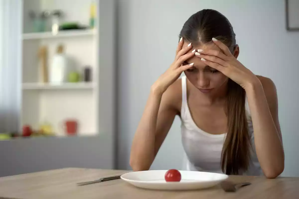 Mujer cabizbaja mirando un tomate en un plato