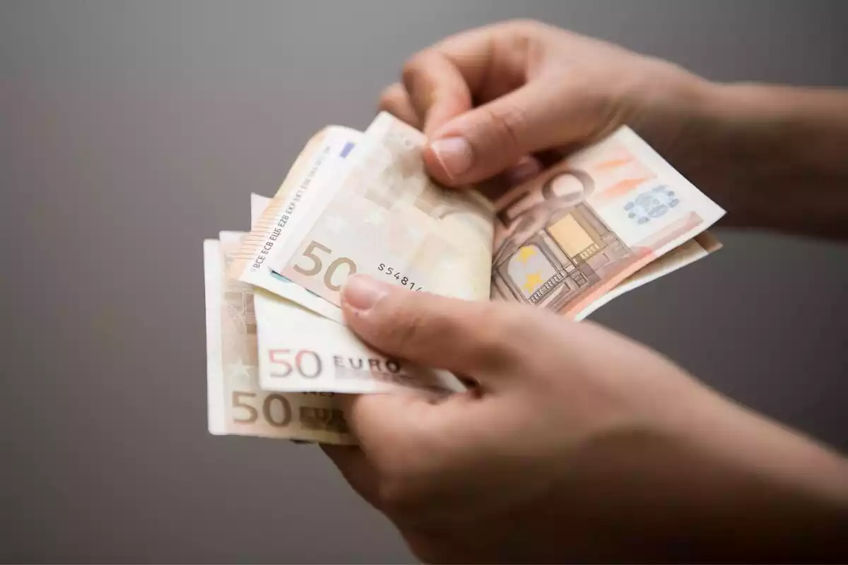 Una persona contando billetes de 50 euros con fondo oscuro