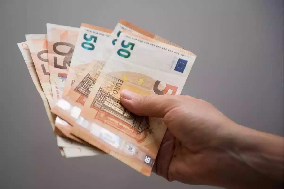 Una mano sujetando billetes de 50 euros con fondo gris