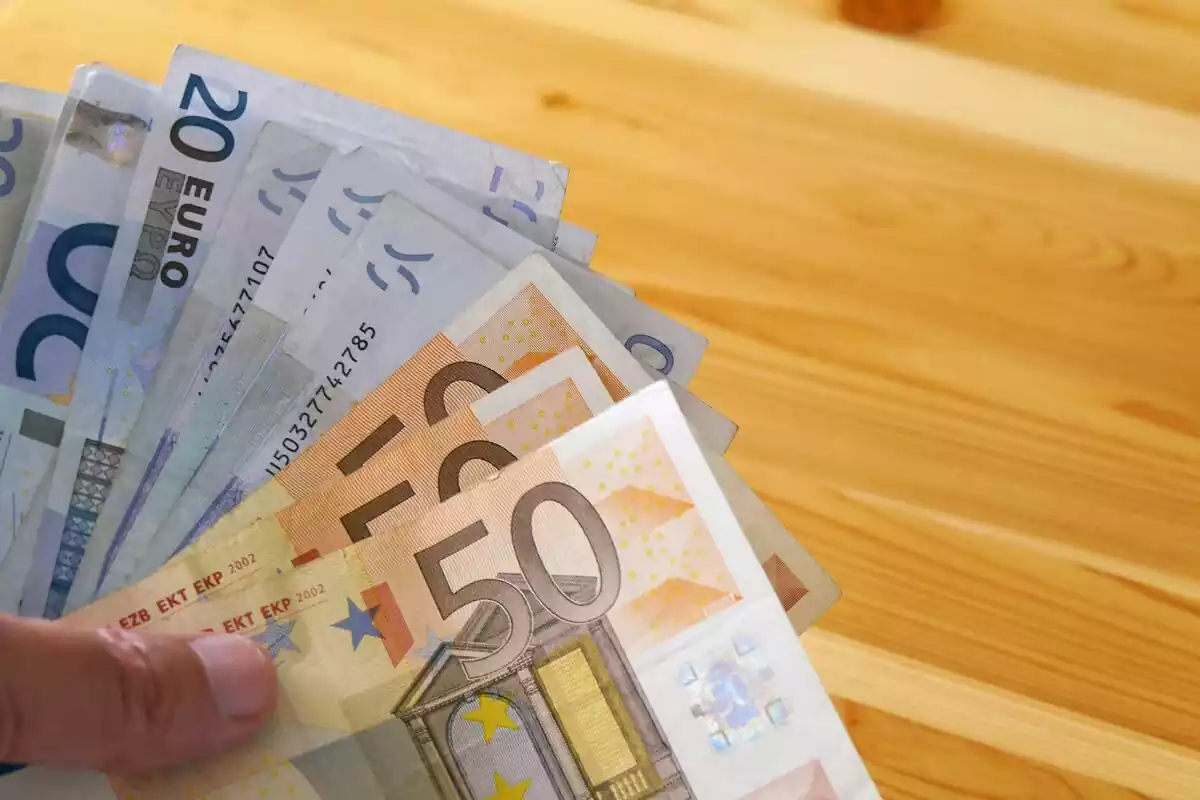 Billetes de 50 y 20 euros en una mano, sobre una mesa de madera