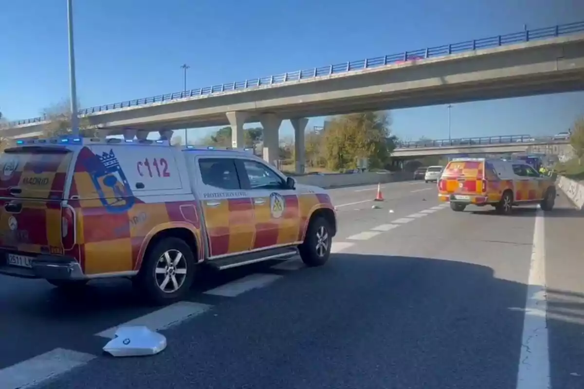 Vehículos de emergencia de Protección Civil en una carretera bajo un puente, con conos de tráfico señalizando el área. Vehículos de emergencia de Protección Civil en una carretera bajo un puente, con conos de tráfico señalizando el área.