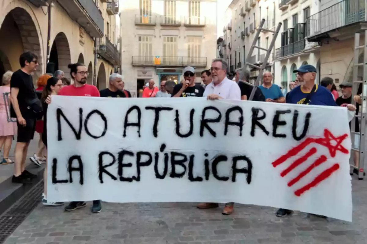 Un grupo de personas sostiene una pancarta blanca con el mensaje No aturareu la república escrito en letras negras y un símbolo rojo en una calle de una ciudad