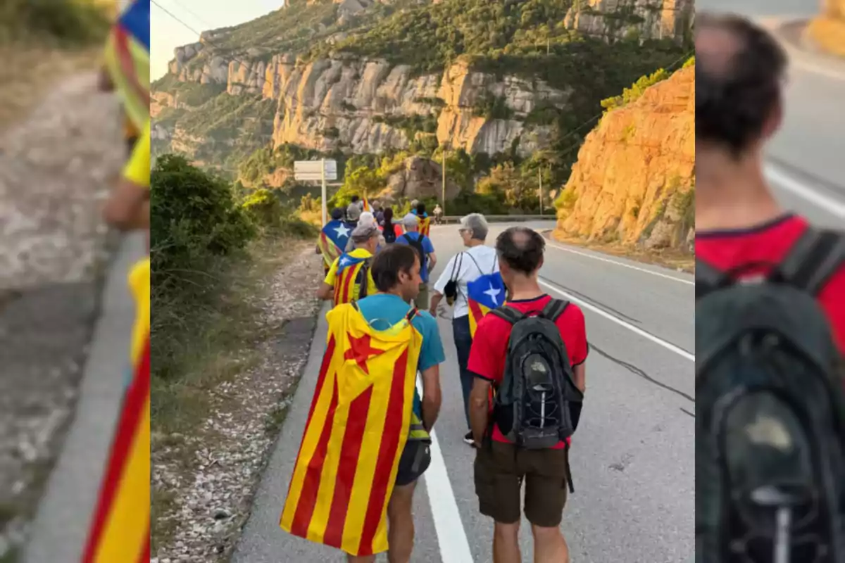 Grupo de personas caminando por una carretera de montaña, algunas llevan banderas esteladas sobre los hombros