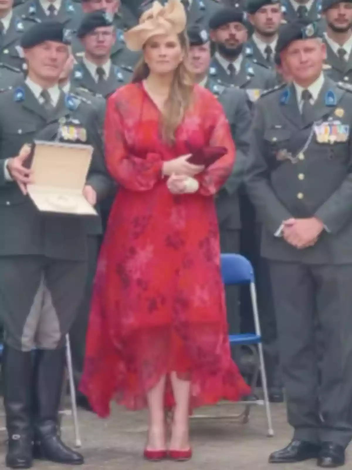 Mujer con vestido rojo y sombrero elegante posando junto a dos hombres uniformados en un evento oficial Mujer con vestido rojo y sombrero elegante posando junto a dos hombres uniformados en un evento oficial