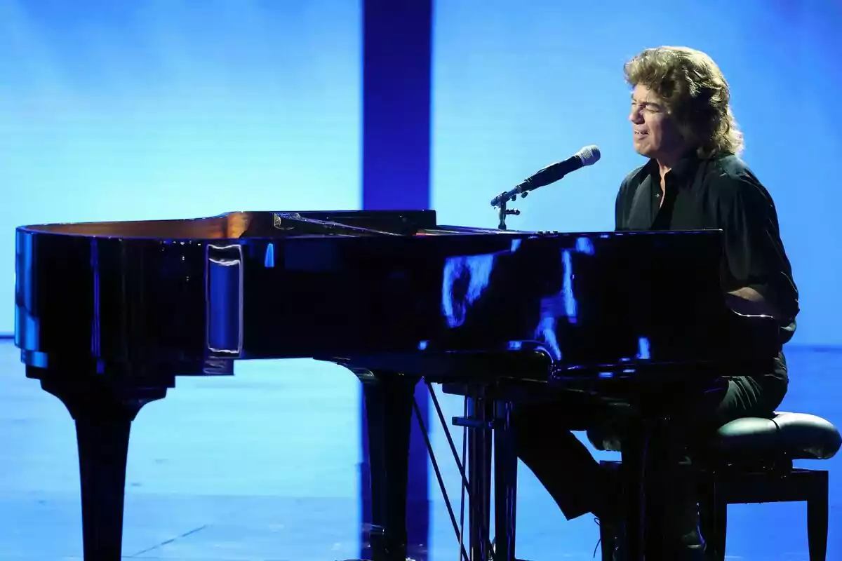 Bertín Osborne tocando el piano de cola y cantando en un escenario iluminado con luz azul de Tu Cara Me Suena Bertín Osborne tocando el piano de cola y cantando en un escenario iluminado con luz azul de Tu Cara Me Suena