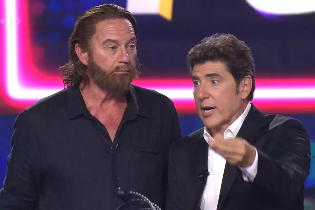 Bertín Osborne y Manel Fuentes en un set de Tu Cara Me Suena con luces de colores al fondo uno de ellos gesticulando mientras habla Bertín Osborne y Manel Fuentes en un set de Tu Cara Me Suena con luces de colores al fondo uno de ellos gesticulando mientras habla