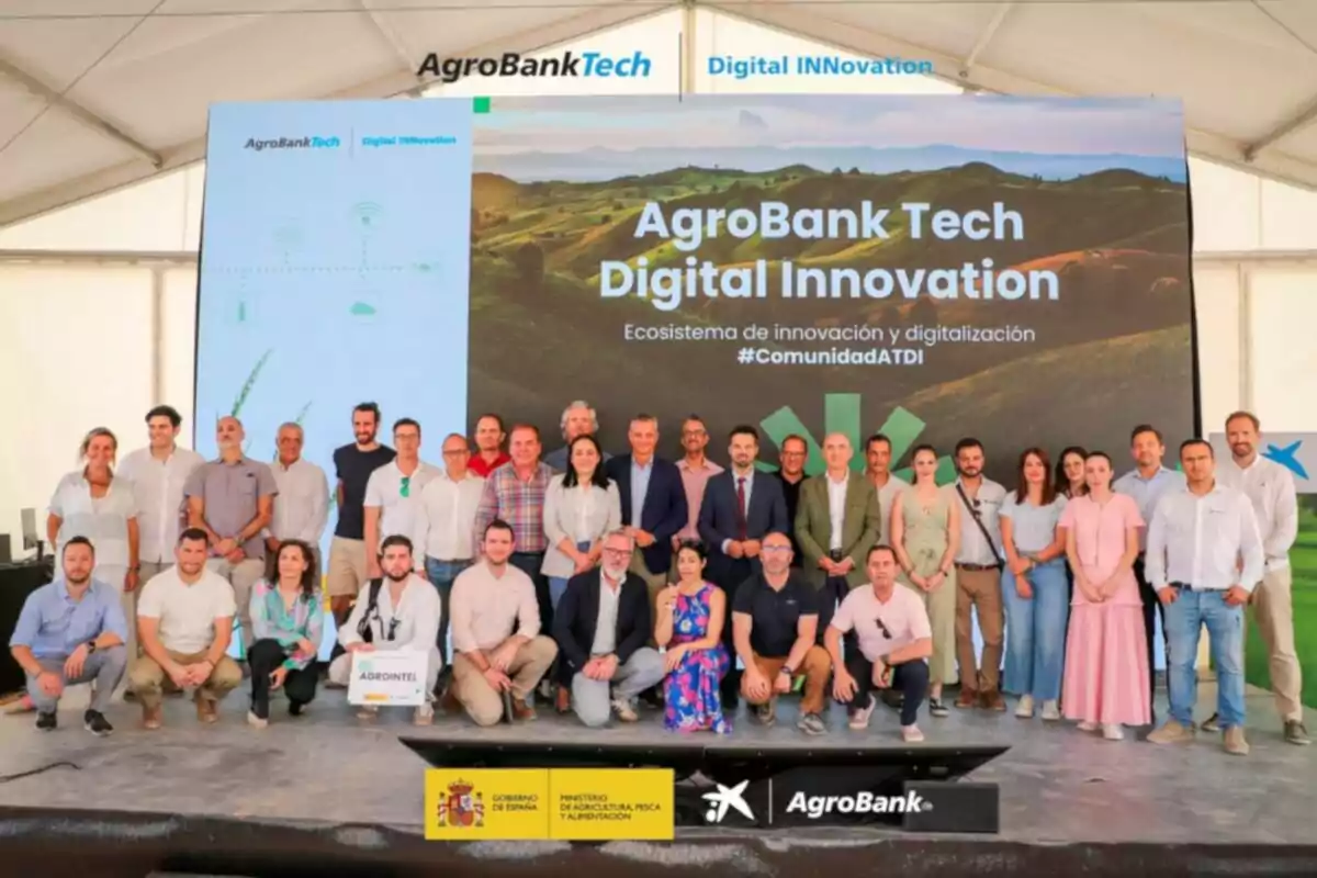 Grupo de personas posando frente a un escenario con un cartel de AgroBank Tech Digital Innovation en un evento sobre innovación y digitalización en el sector agrícola Grupo de personas posando frente a un escenario con un cartel de AgroBank Tech Digital Innovation en un evento sobre innovación y digitalización en el sector agrícola