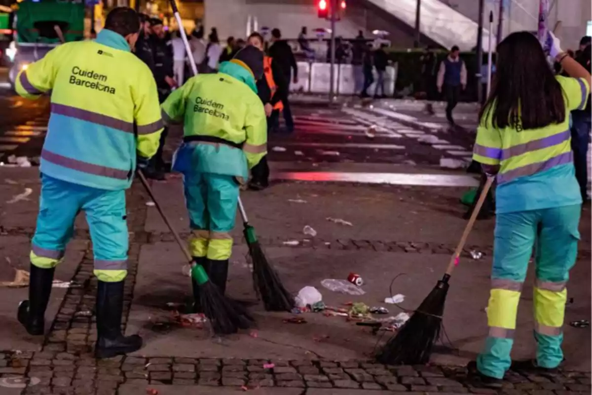 Trabajadores de limpieza con uniformes reflectantes barren basura en una calle durante la noche en Barcelona Trabajadores de limpieza con uniformes reflectantes barren basura en una calle durante la noche en Barcelona