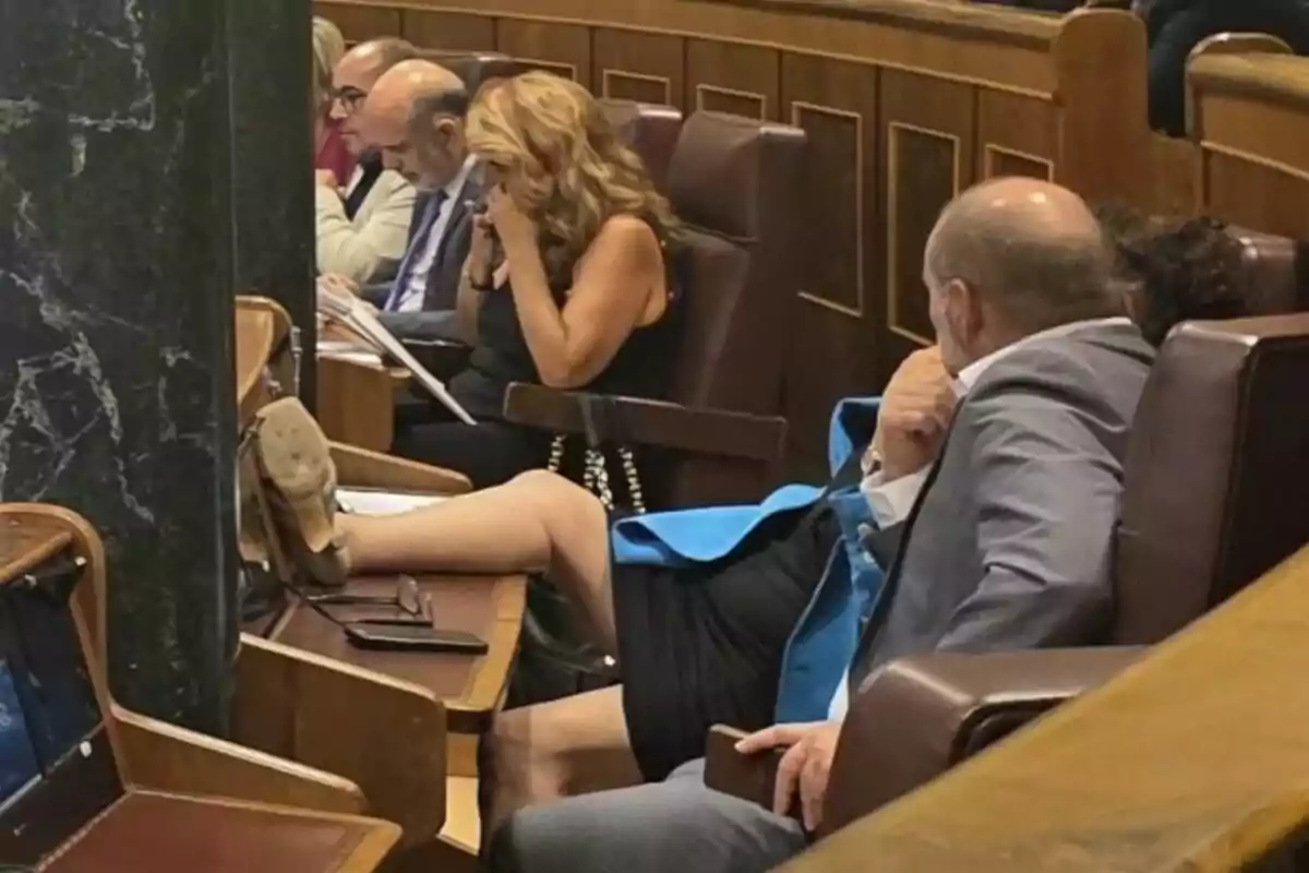 Una persona sentada en una sala de reuniones con la pierna extendida sobre el escritorio mientras otras personas están concentradas en sus documentos. Una persona sentada en una sala de reuniones con la pierna extendida sobre el escritorio mientras otras personas están concentradas en sus documentos.