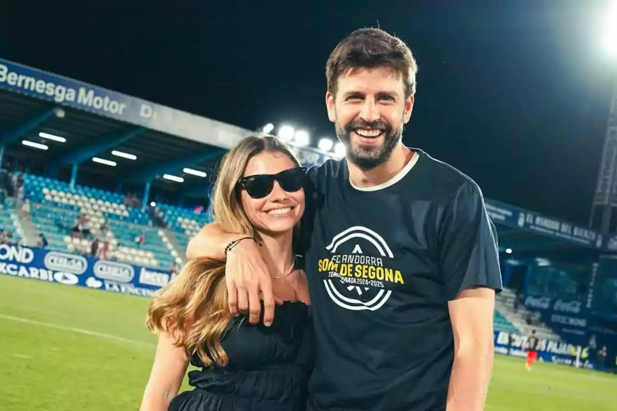 Una pareja sonríe abrazada en un estadio de fútbol con gradas azules y camisetas casuales Una pareja sonríe abrazada en un estadio de fútbol con gradas azules y camisetas casuales