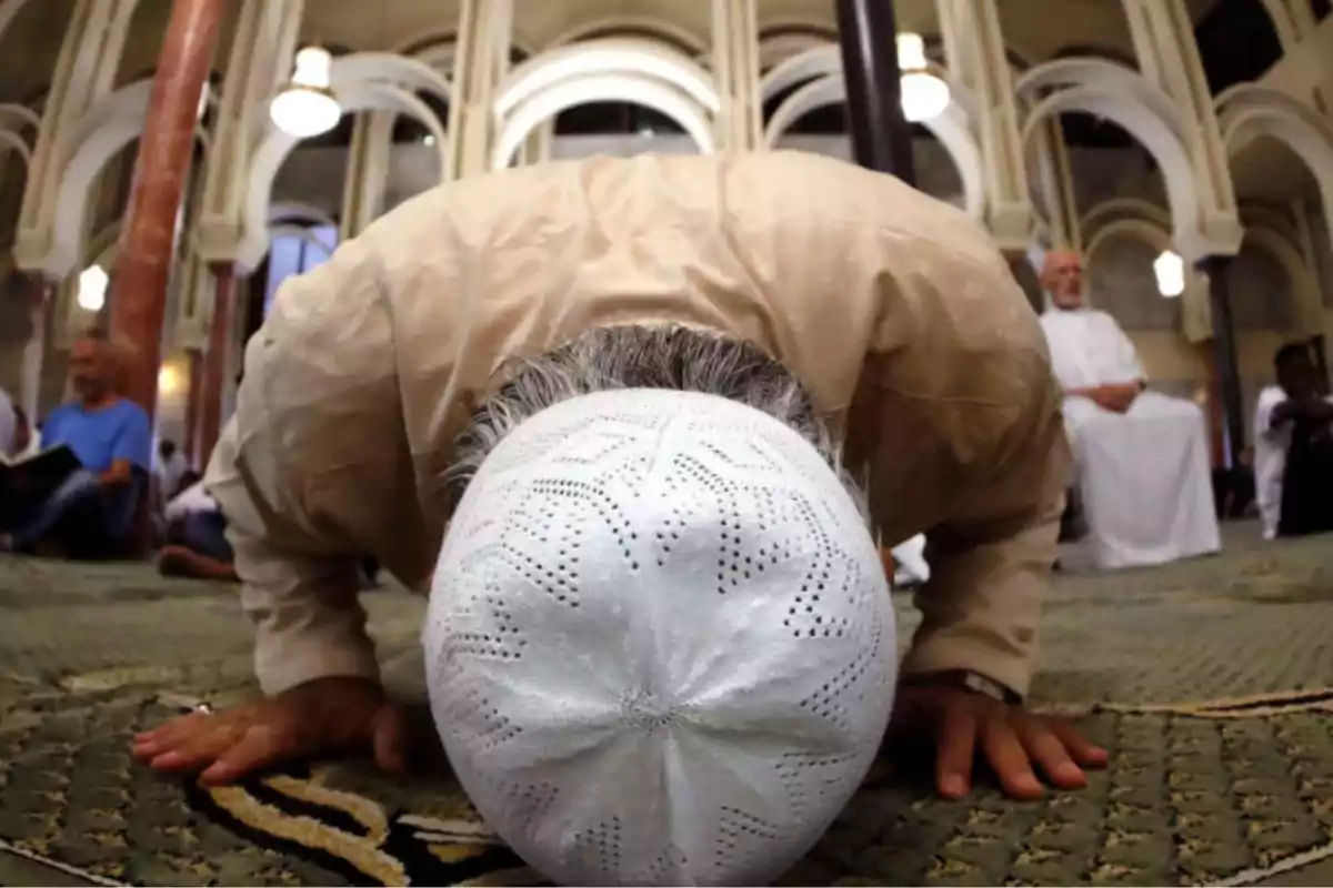 Hombre rezando en una mezquita con la frente tocando el suelo y usando un gorro blanco Hombre rezando en una mezquita con la frente tocando el suelo y usando un gorro blanco