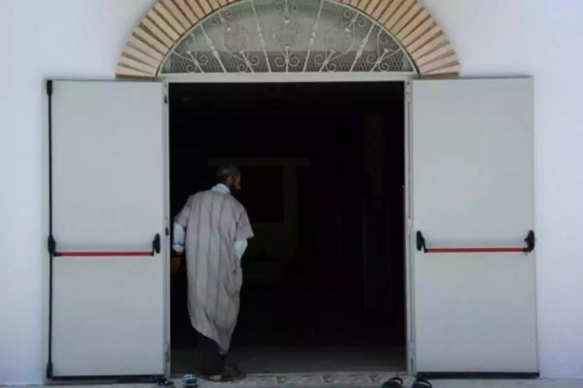 Hombre entrando descalzo a un edificio de puertas abiertas con arco decorativo en la parte superior Hombre entrando descalzo a un edificio de puertas abiertas con arco decorativo en la parte superior