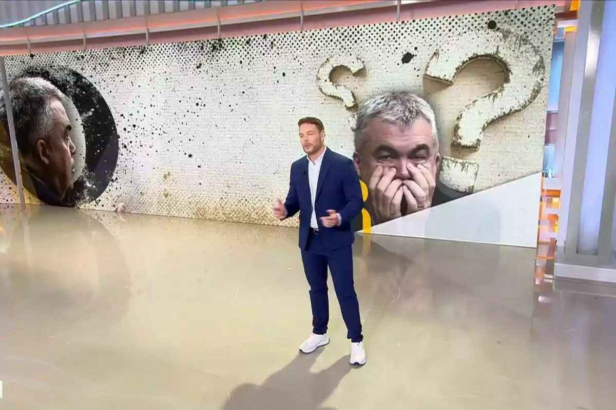 Un presentador de televisión, Jano Mecha, de pie en 'El programa de Ana Rosa' con un fondo que muestra la imagen de Santos Cerdán pensativo y signos de interrogación grandes Un presentador de televisión, Jano Mecha, de pie en 'El programa de Ana Rosa' con un fondo que muestra la imagen de Santos Cerdán pensativo y signos de interrogación grandes