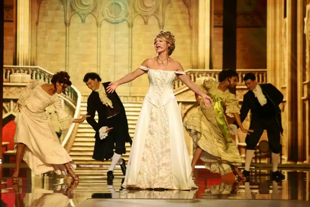 Laura Escanes con vestido elegante canta en el centro de un escenario mientras cuatro bailarines con trajes de época la rodean en un ambiente que simula un palacio antiguo en Tu Cara Me Suena Laura Escanes con vestido elegante canta en el centro de un escenario mientras cuatro bailarines con trajes de época la rodean en un ambiente que simula un palacio antiguo en Tu Cara Me Suena