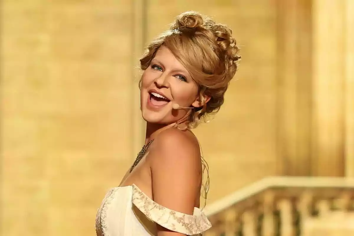 Laura Escanes con vestido elegante y micrófono de diadema sonriendo en un escenario iluminado en Tu Cara Me Suena