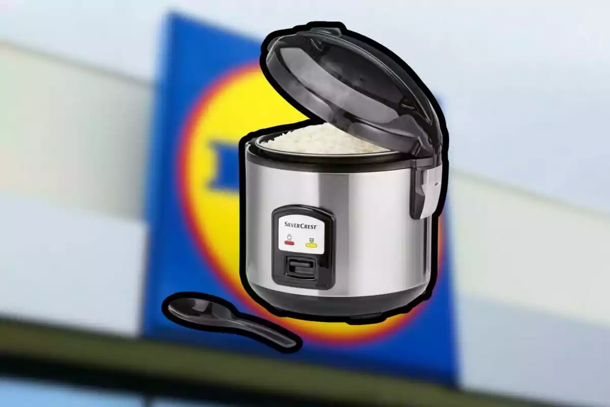 Arrocera eléctrica de acero inoxidable con tapa abierta y arroz cocido al frente de un letrero borroso de supermercado Arrocera eléctrica de acero inoxidable con tapa abierta y arroz cocido al frente de un letrero borroso de supermercado