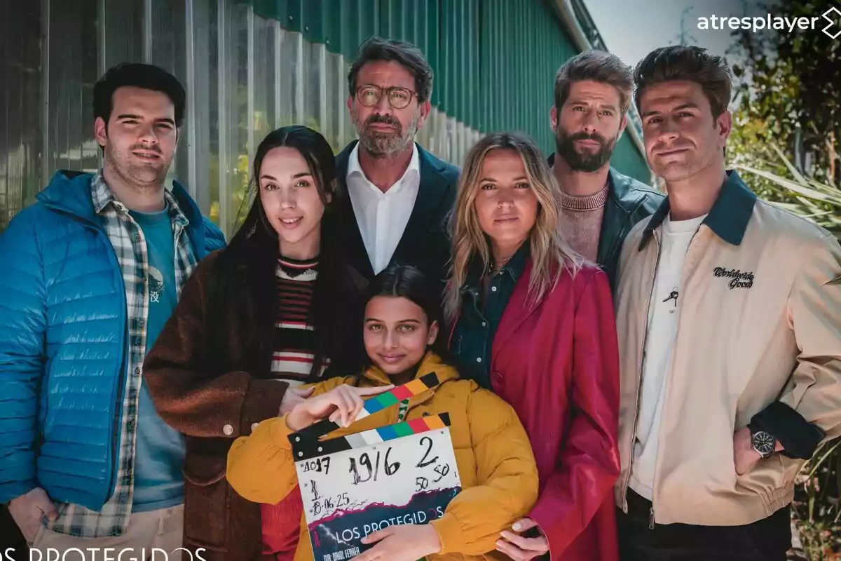 Ana Fernández, Luis Fernández, Mario Marzo, Antonio Garrido, Daniel Avilés, Maggie García y Cosette Silguero posan juntas al aire libre, una de ellas sostiene una claqueta de cine y todos miran a la cámara con expresión relajada de Los Protegidos.