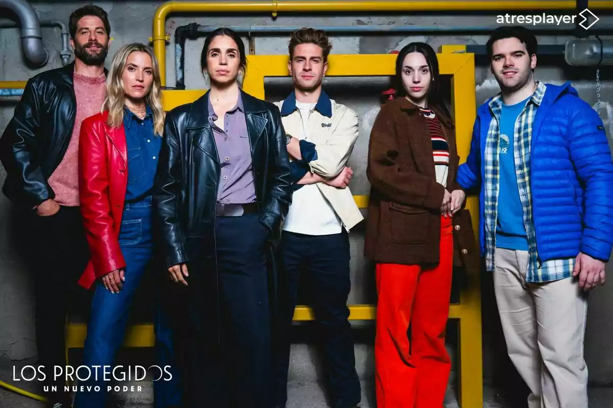 Ana Fernández, Luis Fernández, Mario Marzo, Elena Furiase, Daniel Avilés y Maggie García posan juntas frente a una pared gris con tuberías amarillas, todas vestidas con ropa casual y abrigos coloridos, bajo el logo de una serie llamada Los Protegidos Un Nuevo Poder y el logotipo de atresplayer en la esquina superior derecha. Ana Fernández, Luis Fernández, Mario Marzo, Elena Furiase, Daniel Avilés y Maggie García posan juntas frente a una pared gris con tuberías amarillas, todas vestidas con ropa casual y abrigos coloridos, bajo el logo de una serie llamada Los Protegidos Un Nuevo Poder y el logotipo de atresplayer en la esquina superior derecha.