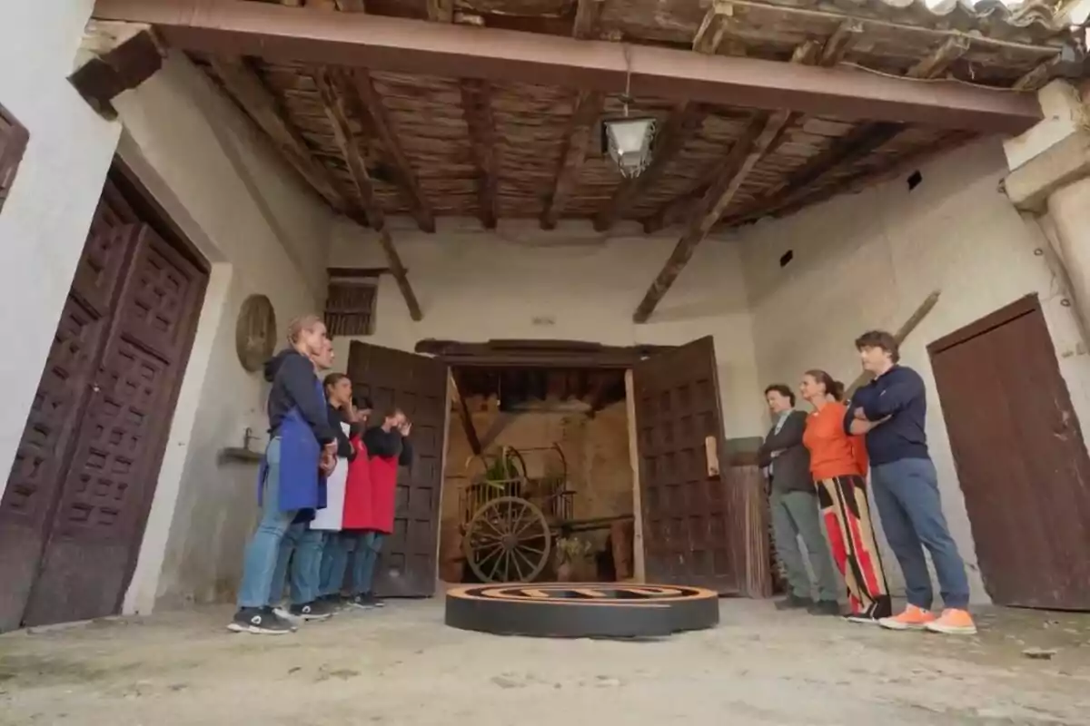 Un grupo de personas divididas en dos equipos se encuentra en un patio rústico frente a tres jueces, con una carreta antigua al fondo y un techo de madera expuesta en 'MasterChef'. Un grupo de personas divididas en dos equipos se encuentra en un patio rústico frente a tres jueces, con una carreta antigua al fondo y un techo de madera expuesta en 'MasterChef'.