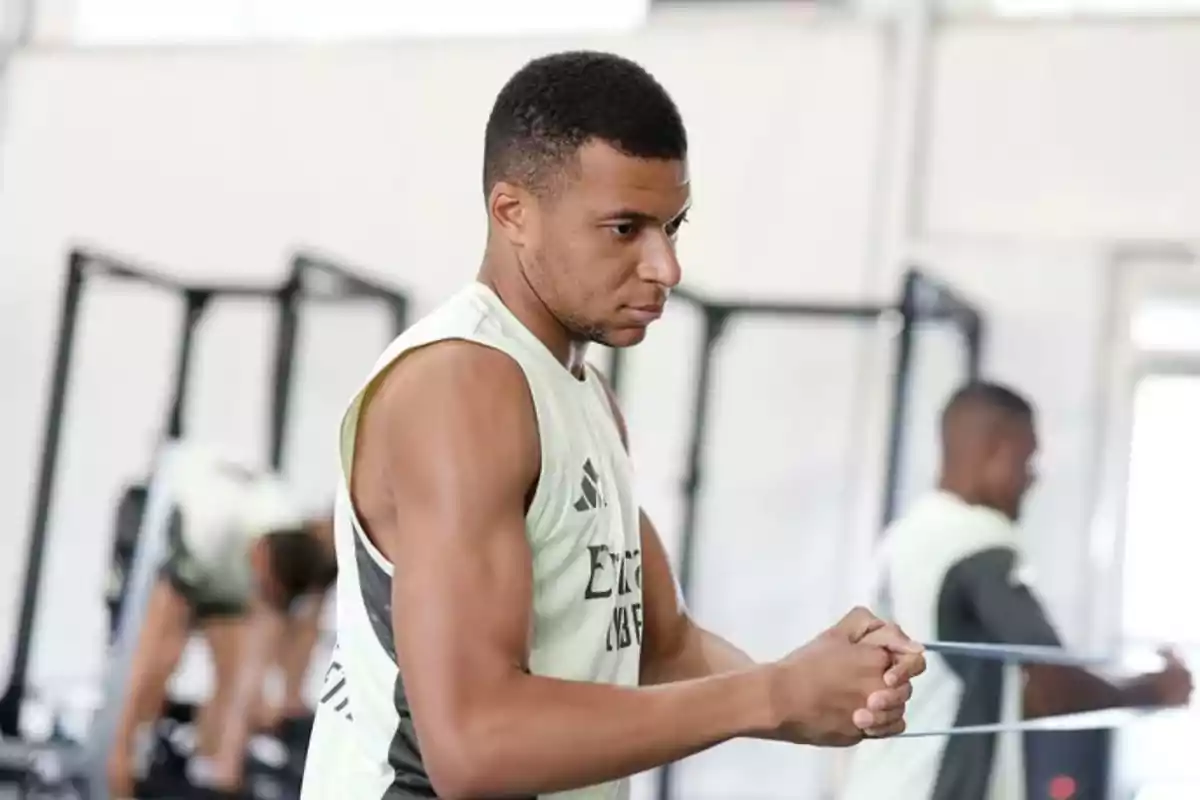 Joven deportista entrenando con banda elástica en un gimnasio mientras otras personas también hacen ejercicio al fondo Joven deportista entrenando con banda elástica en un gimnasio mientras otras personas también hacen ejercicio al fondo