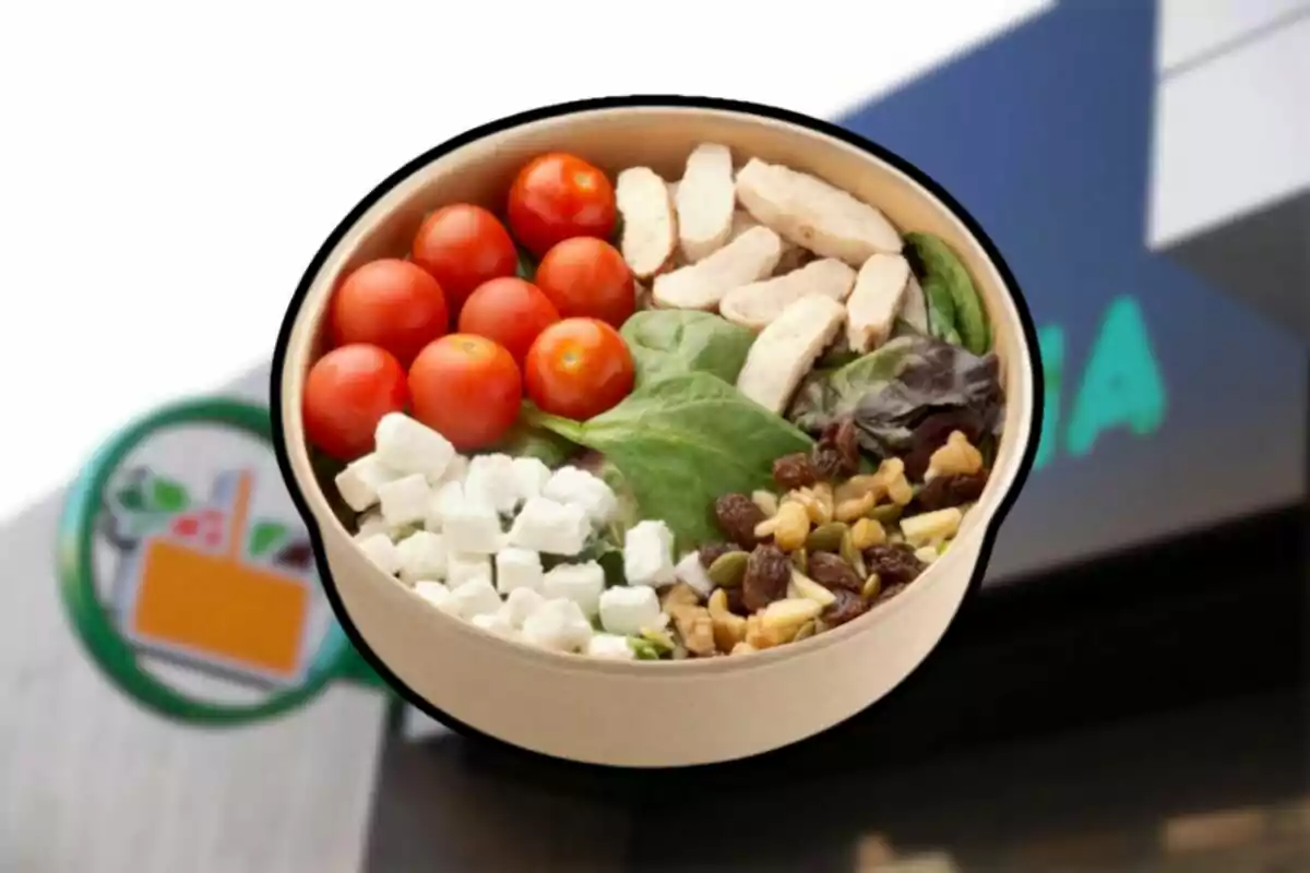 Ensalada en un recipiente de cartón con jitomates cherry, pollo, espinaca, queso y frutos secos frente a una tienda Ensalada en un recipiente de cartón con jitomates cherry, pollo, espinaca, queso y frutos secos frente a una tienda