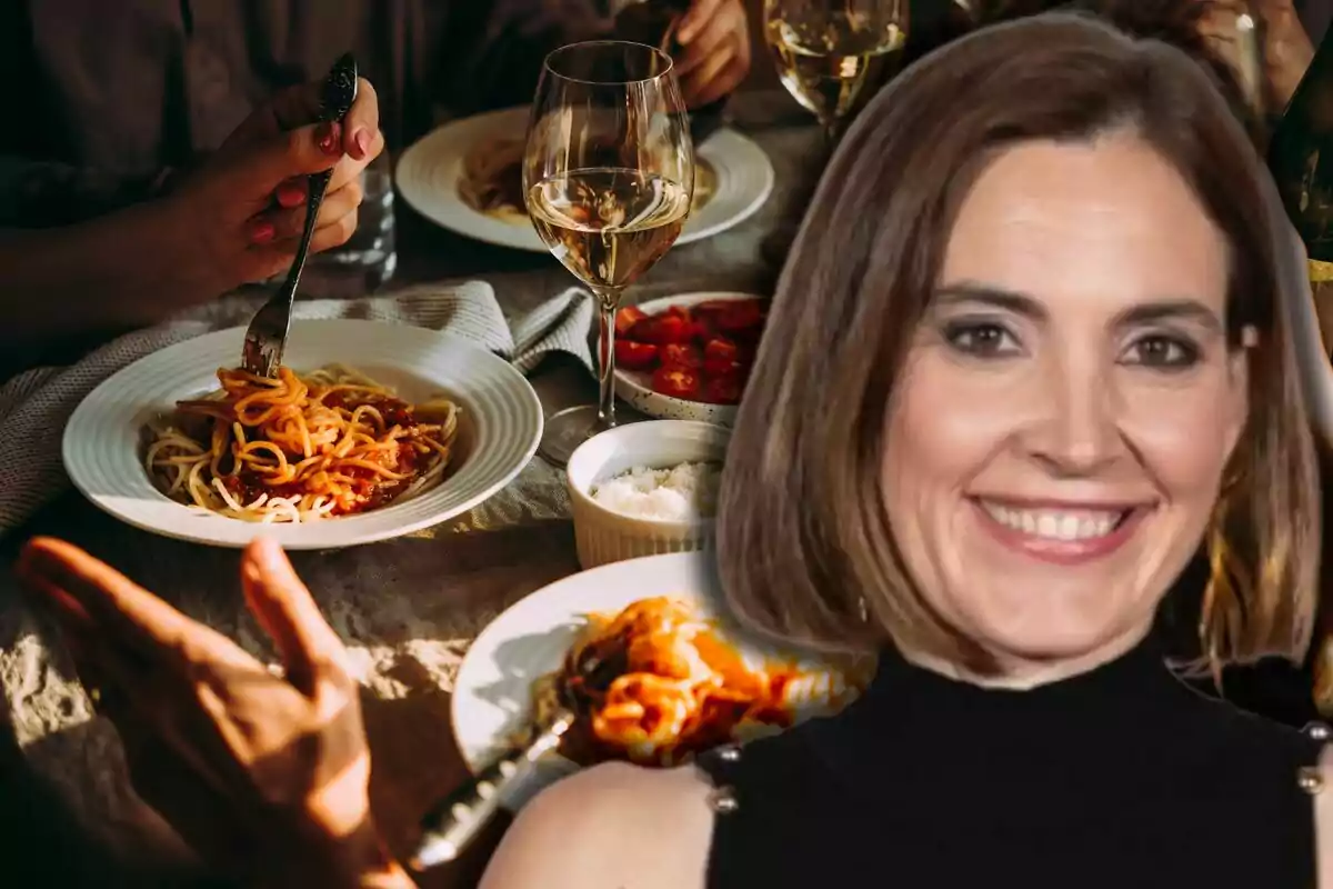 Una mujer sonriente en primer plano con una mesa servida con platos de espaguetis, copas de vino y comida al fondo Una mujer sonriente en primer plano con una mesa servida con platos de espaguetis, copas de vino y comida al fondo