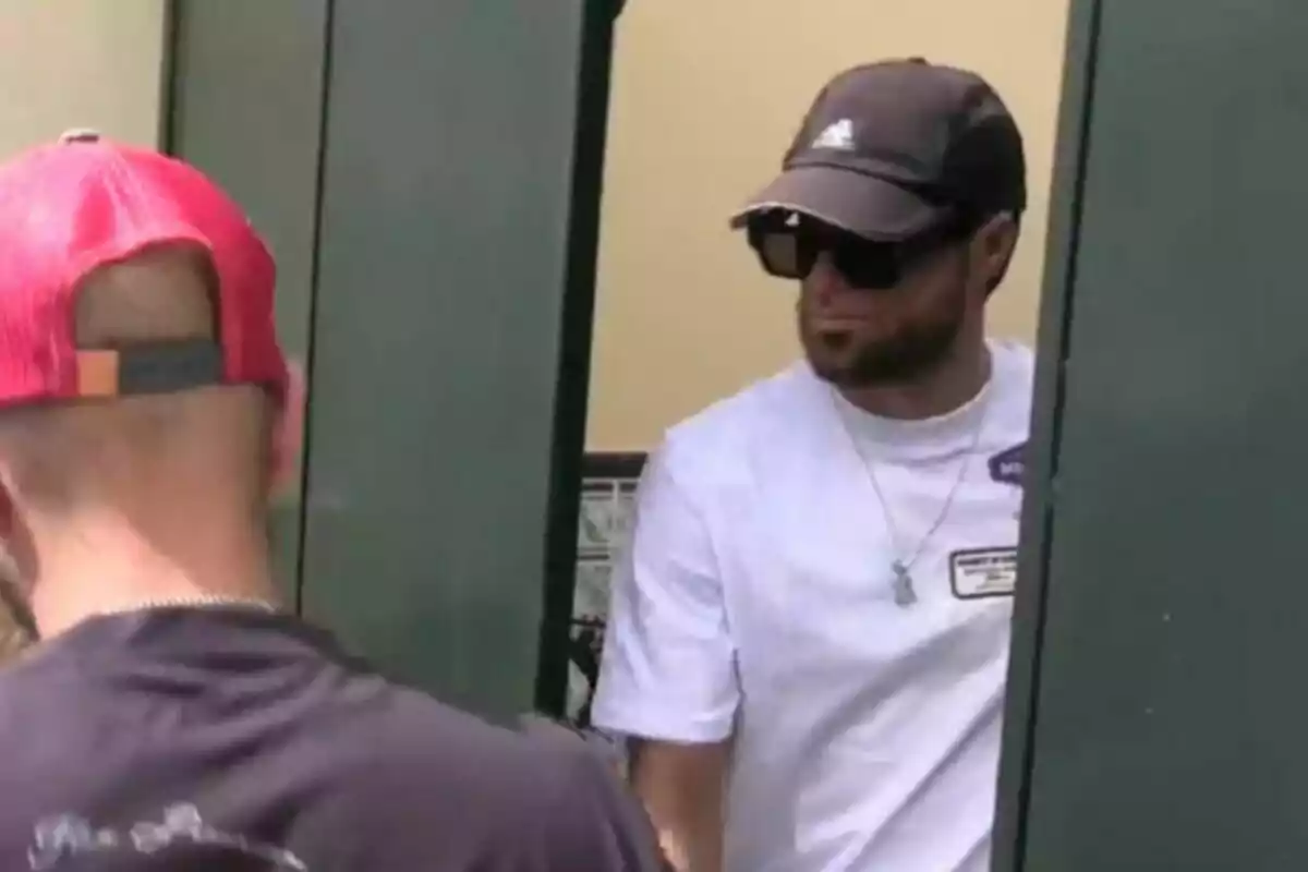 Montoya con gorra, gafass de sol y camiseta casual está cerca de una puerta verde.