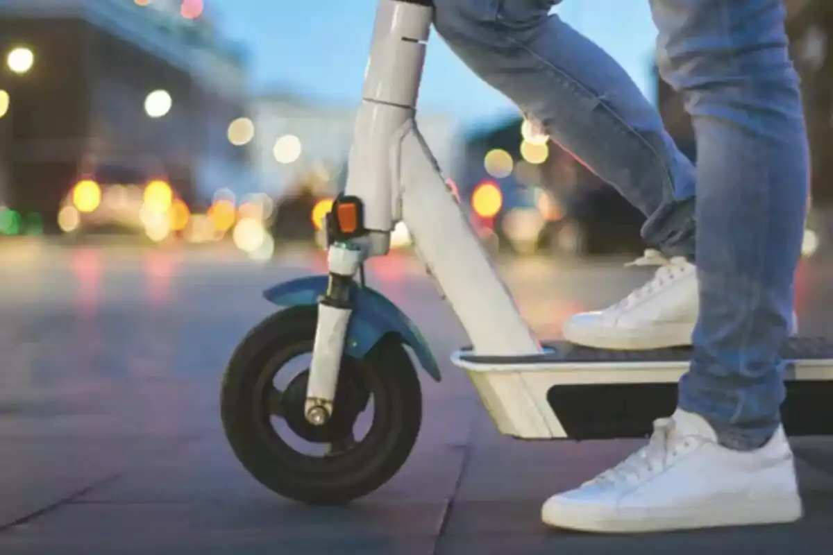 Persona usando un patinete eléctrico en una ciudad al atardecer con luces desenfocadas de fondo