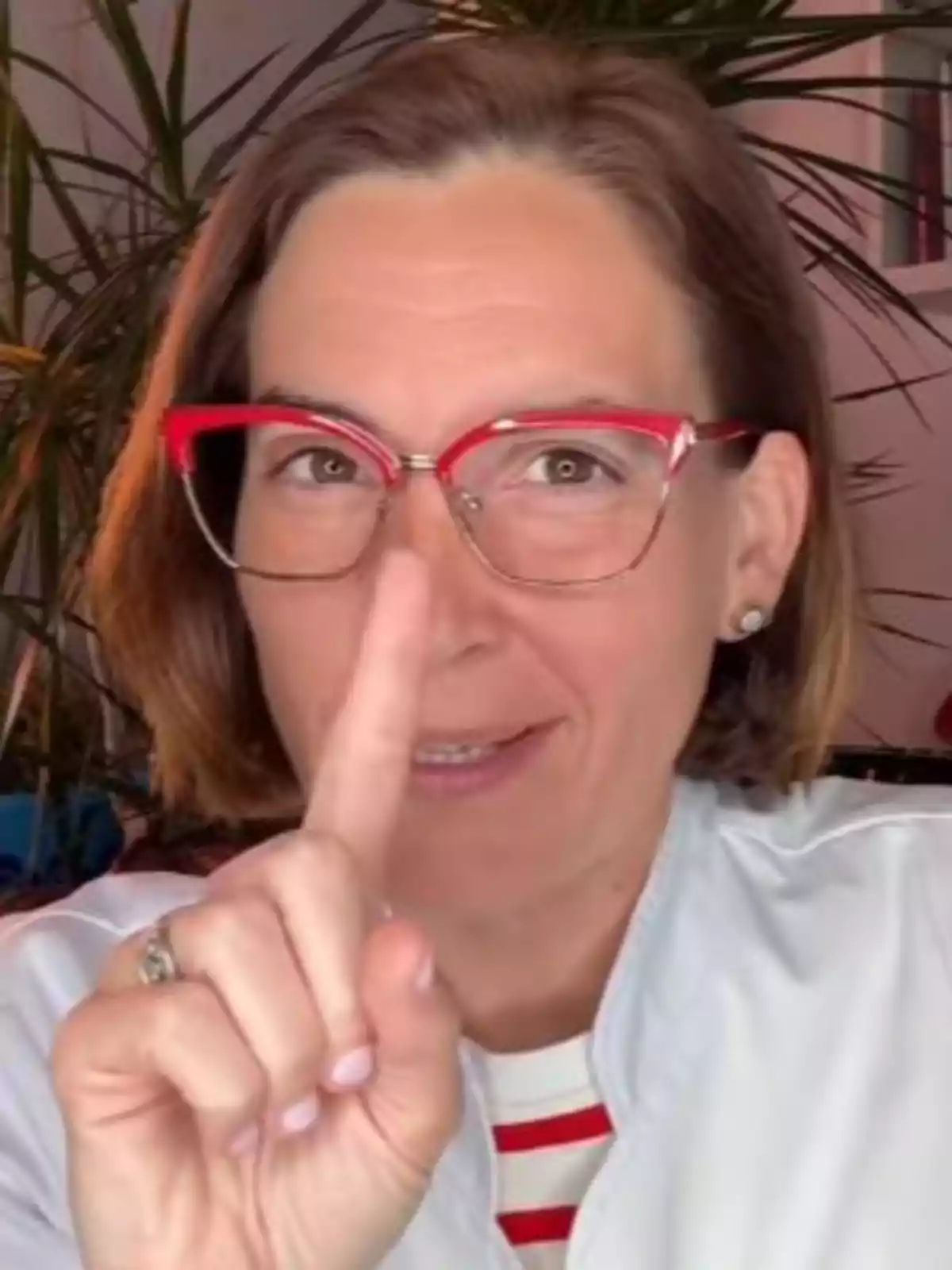 Mujer con gafas rojas señalando hacia arriba con el dedo índice y sonriendo Mujer con gafas rojas señalando hacia arriba con el dedo índice y sonriendo