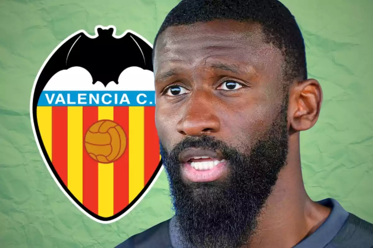 Un hombre con barba en primer plano y el escudo del Valencia Club de Fútbol al fondo sobre un fondo verde.