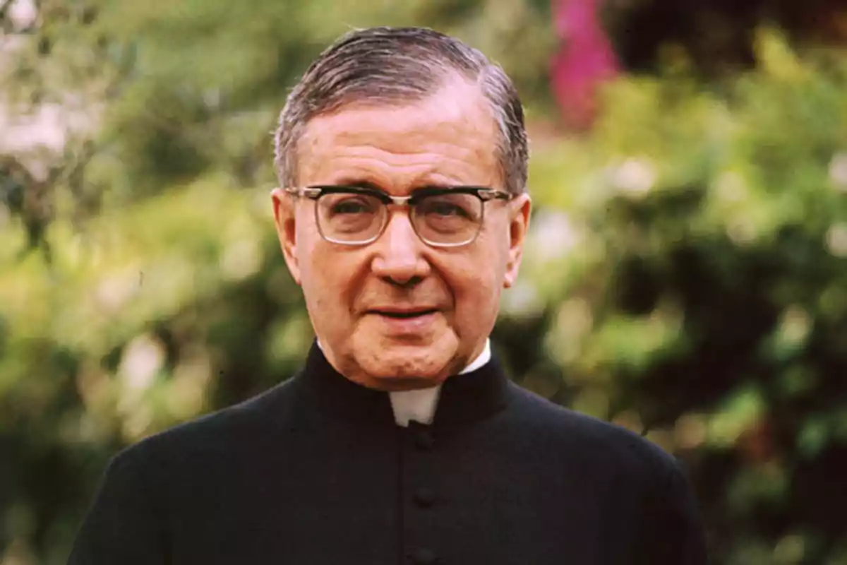 Hombre de mediana edad con gafas y vestimenta clerical negra posando al aire libre con fondo de vegetación desenfocada Hombre de mediana edad con gafas y vestimenta clerical negra posando al aire libre con fondo de vegetación desenfocada
