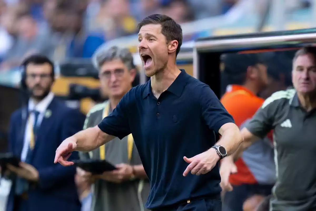 Entrenador de fútbol dando indicaciones en la banda durante un partido con expresión intensa y personas de fondo observando Entrenador de fútbol dando indicaciones en la banda durante un partido con expresión intensa y personas de fondo observando