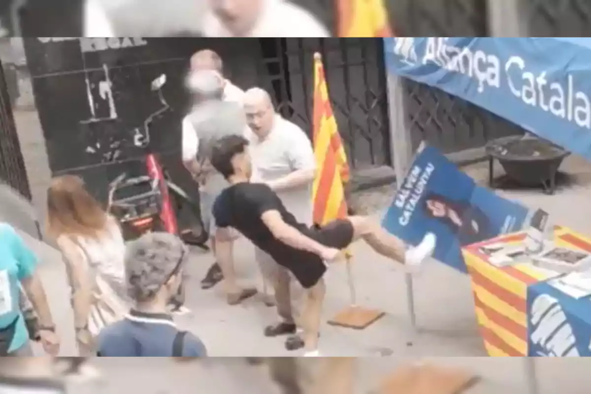 Un joven patea un cartel de propaganda política junto a una mesa decorada con la bandera catalana en una calle concurrida