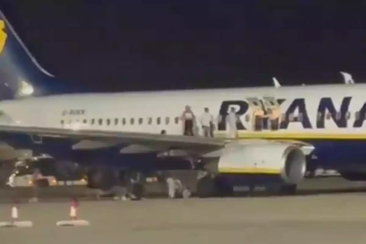 Personas de pie sobre el ala de un avión de Ryanair en la pista durante la noche. Personas de pie sobre el ala de un avión de Ryanair en la pista durante la noche.