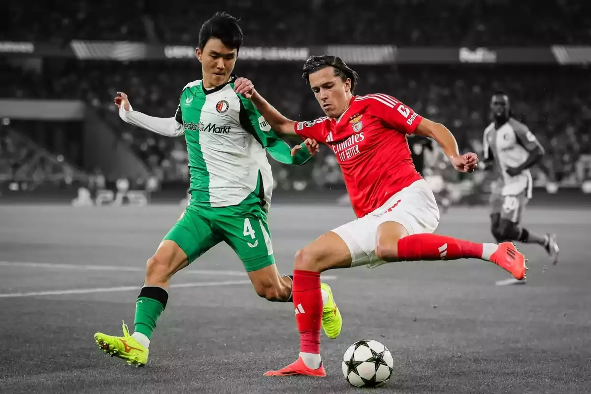 Dos futbolistas disputan el balón durante un partido en un estadio lleno de espectadores Dos futbolistas disputan el balón durante un partido en un estadio lleno de espectadores