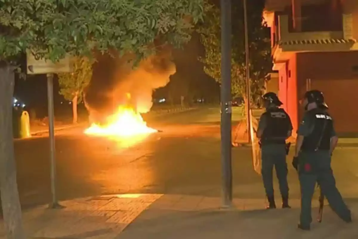 Dos agentes de policía observan un incendio en medio de una calle durante la noche