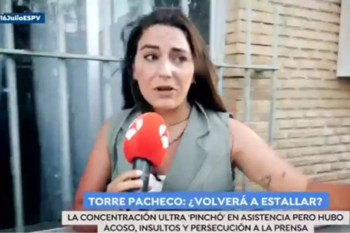 Reportera con micrófono rojo informando en la calle frente a una pared de ladrillo, con un cintillo de noticias en la parte inferior de la imagen. Captura de 'Espejo Público' Reportera con micrófono rojo informando en la calle frente a una pared de ladrillo, con un cintillo de noticias en la parte inferior de la imagen. Captura de 'Espejo Público'