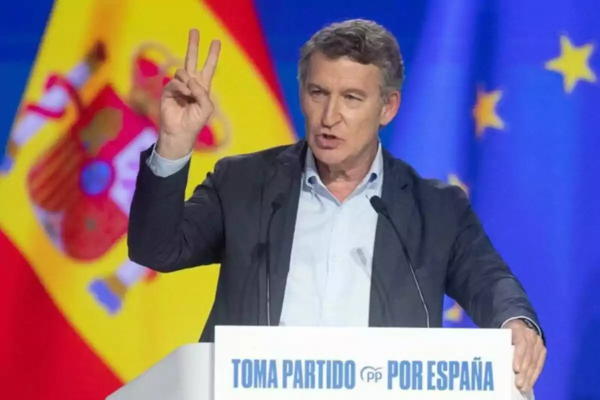 Hombre hablando en un atril con el texto Toma Partido por España haciendo un gesto con la mano y banderas de España y la Unión Europea de fondo