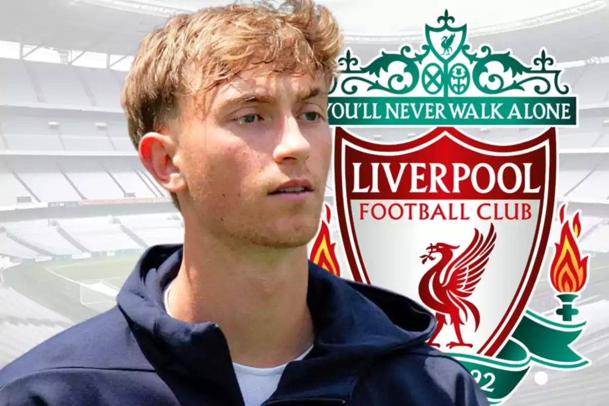 Joven con chaqueta oscura frente al escudo del Liverpool Football Club en un estadio vacío