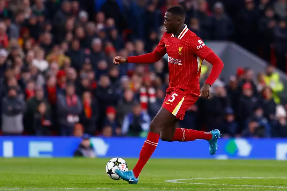 Futbolista del Liverpool con uniforme rojo controla el balón durante un partido en un estadio lleno de espectadores Futbolista del Liverpool con uniforme rojo controla el balón durante un partido en un estadio lleno de espectadores