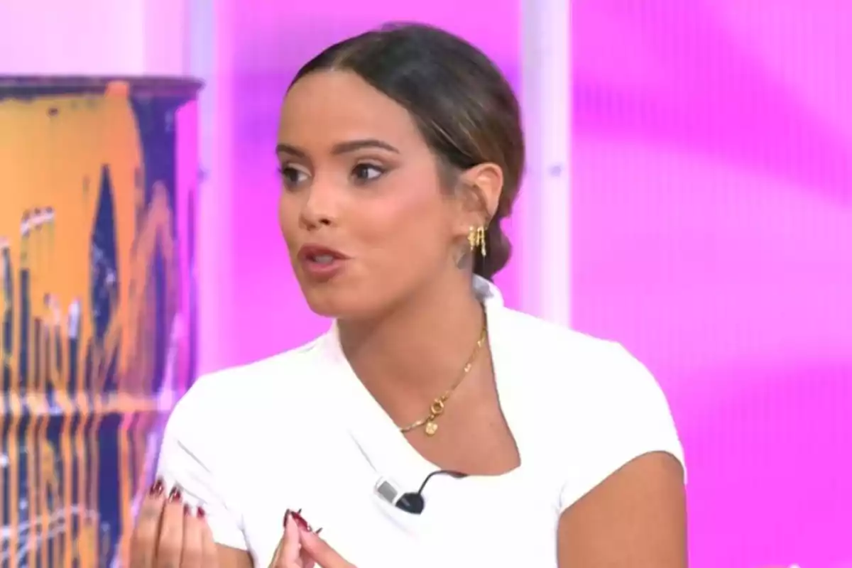 Gloria Camila joven de cabello recogido y vestida de blanco hablando en un set de televisión con fondo rosa Gloria Camila joven de cabello recogido y vestida de blanco hablando en un set de televisión con fondo rosa