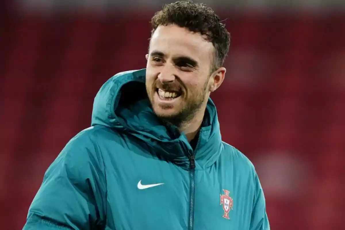 Diogo Jota con chaqueta deportiva verde agua y escudo de Portugal sonriendo en un estadio