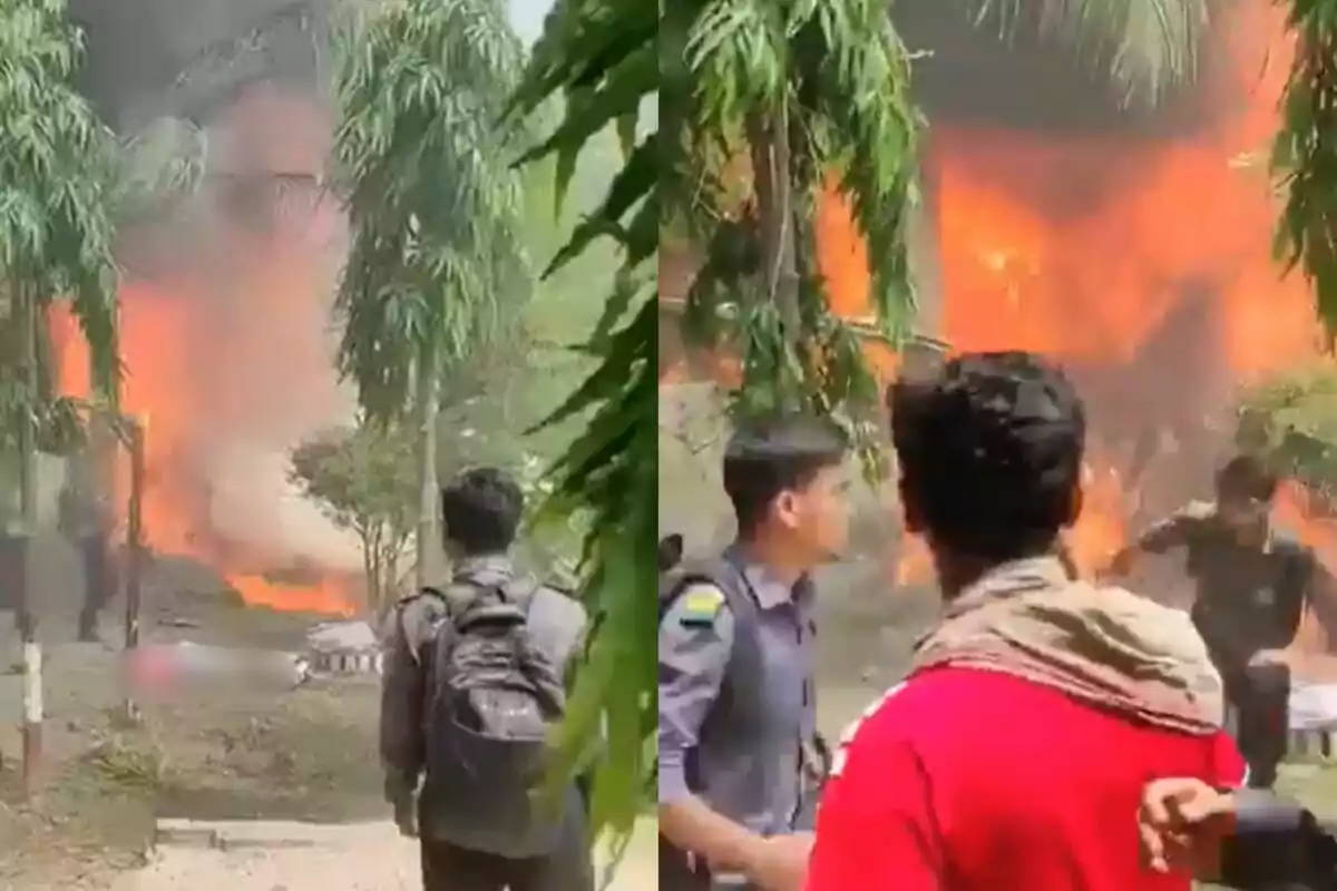 Varias personas observan un incendio de gran magnitud en una zona arbolada durante el día, con llamas y humo visibles al fondo.
