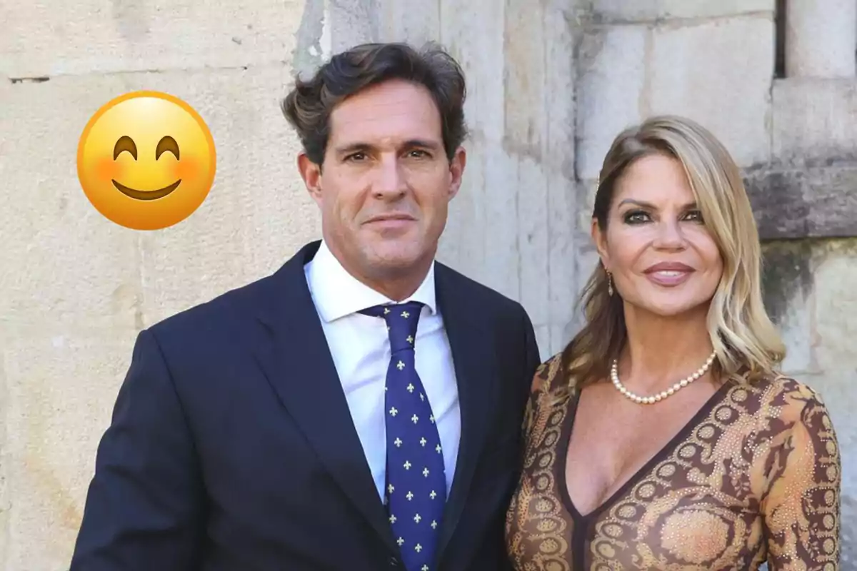 Makoke y Gonzalo elegantemente vestida posando frente a una pared de piedra con un emoji sonriente grande a la izquierda