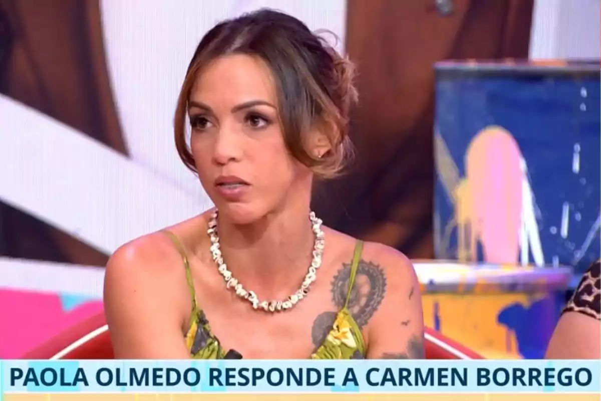 Paola Olmedo con vestido verde y collar de conchas sentada en un plató de televisión con un rótulo que dice Paola Olmedo responde a Carmen Borrego Paola Olmedo con vestido verde y collar de conchas sentada en un plató de televisión con un rótulo que dice Paola Olmedo responde a Carmen Borrego