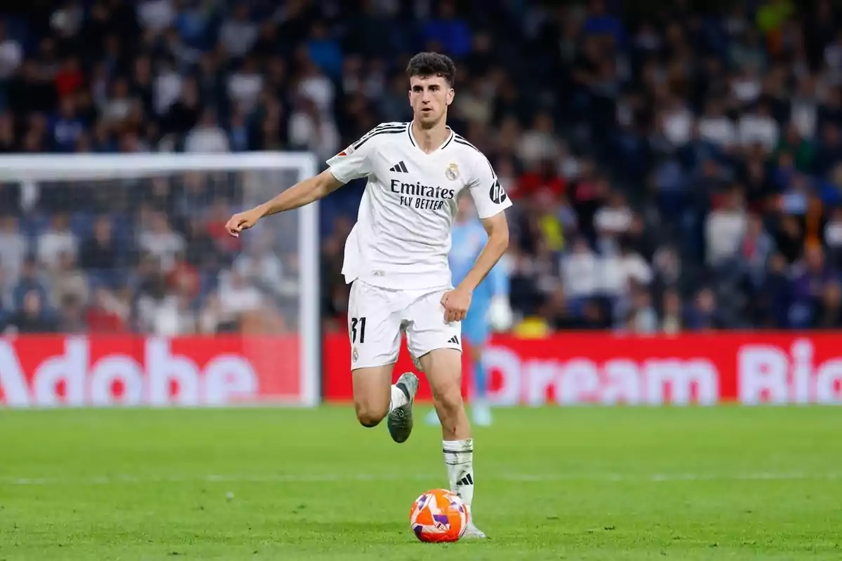 Futbolista del Real Madrid con uniforme blanco controlando el balón durante un partido en un estadio lleno de espectadores Futbolista del Real Madrid con uniforme blanco controlando el balón durante un partido en un estadio lleno de espectadores
