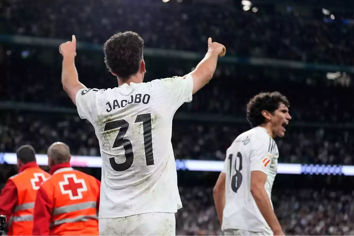 Futbolista con el número 31 y el nombre Jacobo celebra con los brazos en alto mientras otro jugador grita emocionado en un estadio lleno de aficionados Futbolista con el número 31 y el nombre Jacobo celebra con los brazos en alto mientras otro jugador grita emocionado en un estadio lleno de aficionados