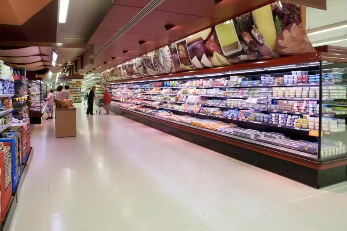 Pasillo de supermercado con vitrinas refrigeradas llenas de productos y varias personas haciendo compras Pasillo de supermercado con vitrinas refrigeradas llenas de productos y varias personas haciendo compras