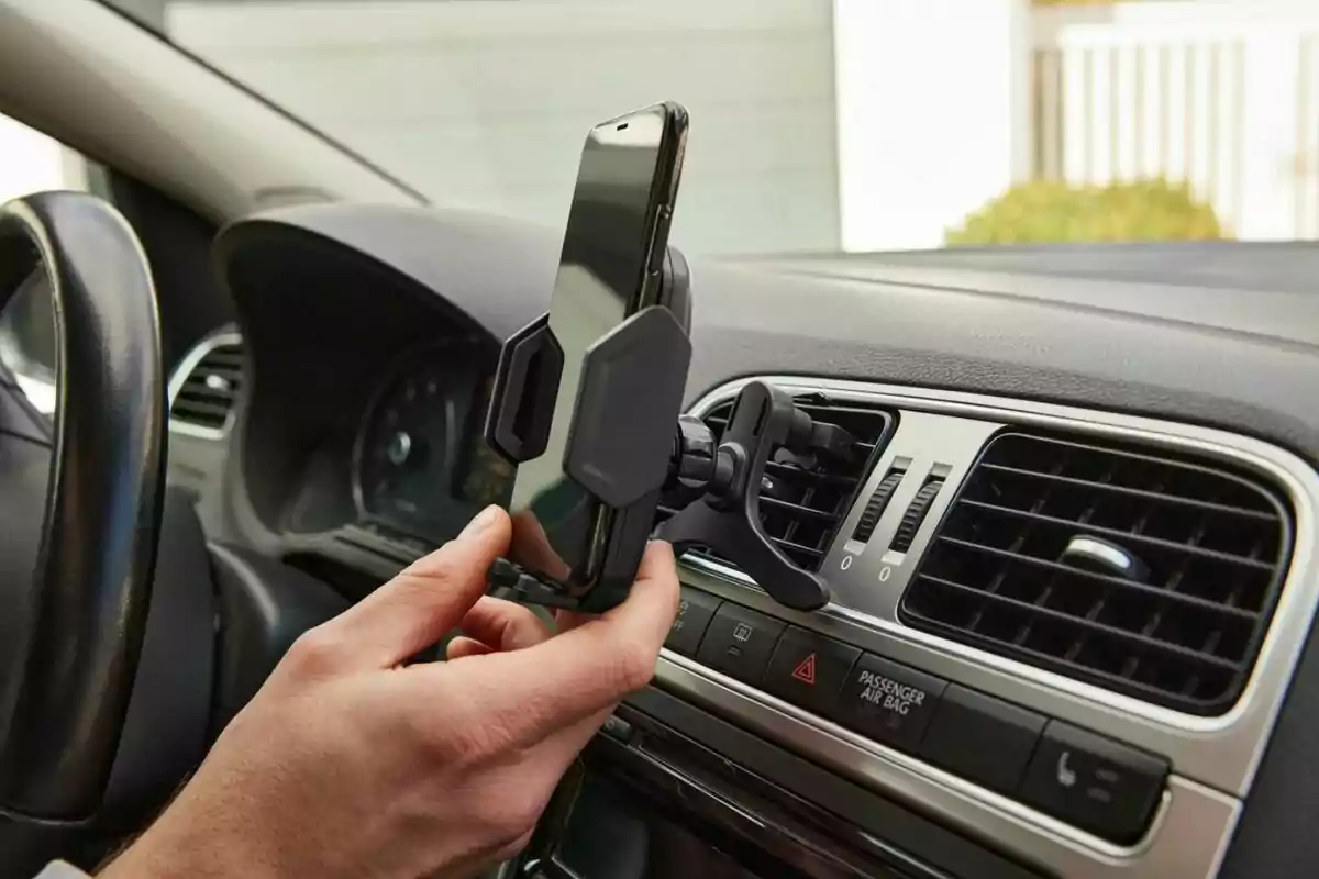 Persona colocando un teléfono móvil en un soporte para auto sujeto a la rejilla de ventilación del tablero. Persona colocando un teléfono móvil en un soporte para auto sujeto a la rejilla de ventilación del tablero.