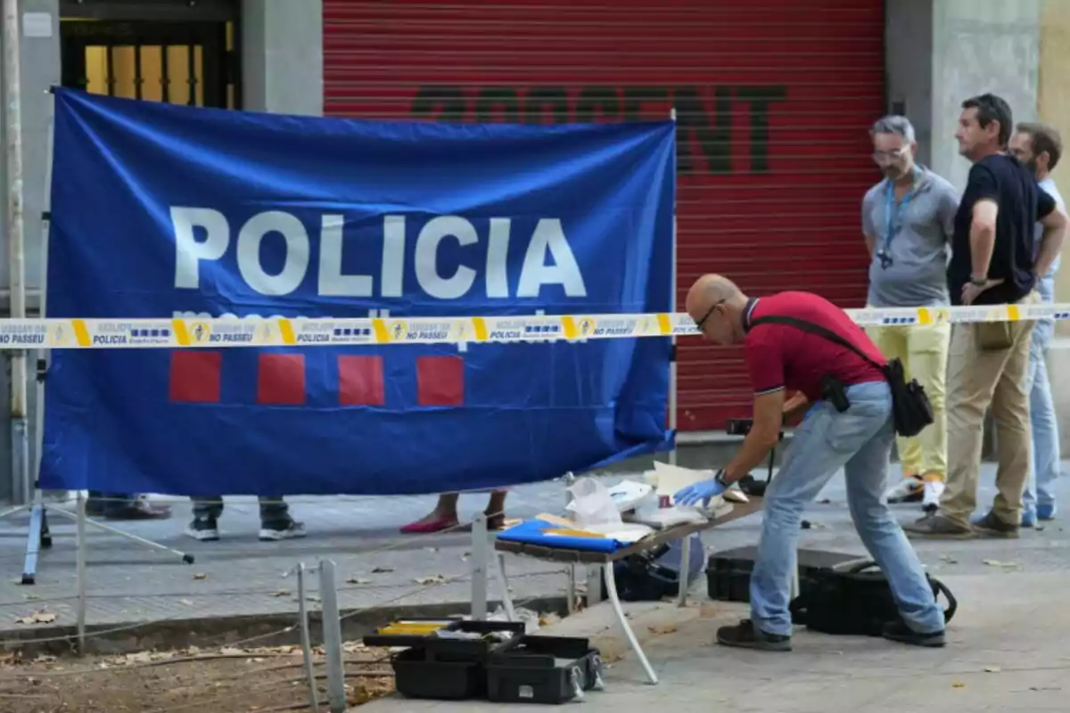 Un agente realiza labores de investigación en una escena acordonada por la policía mientras varias personas observan detrás de una cinta de seguridad Un agente realiza labores de investigación en una escena acordonada por la policía mientras varias personas observan detrás de una cinta de seguridad